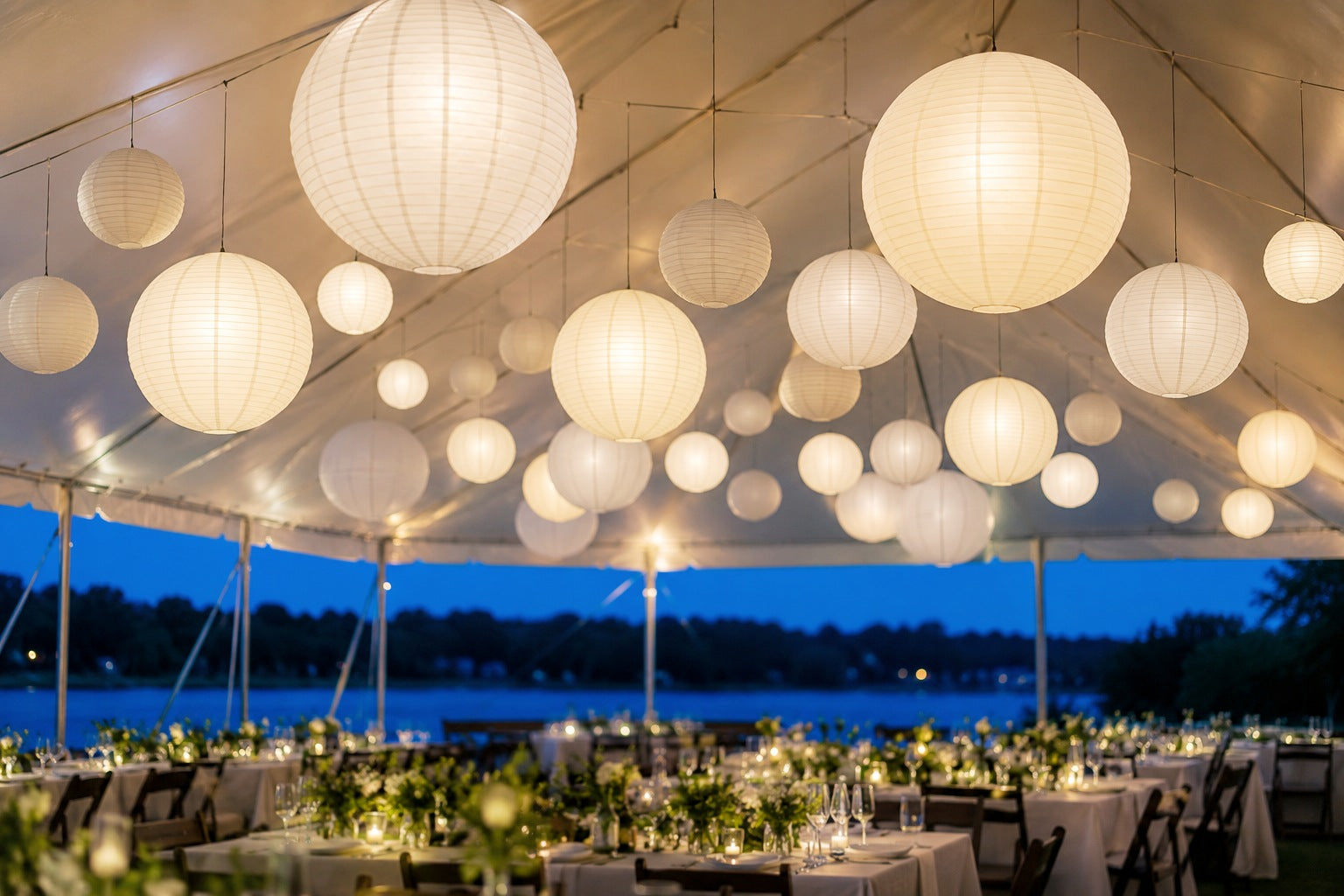 White round paper lanterns in mixed sizes hanging over an outdoor wedding reception at dusk